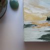 Detail of Painting Landscape sunrise with yellows, greens and taupe on a table next to some gems and a plant