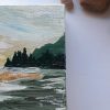 Detail of a Fine Art Sunrise landscape painting with taupe, yellows and greens on a white table next to some stones and a green plant