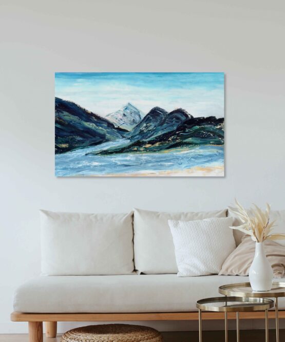 Abstract impressionist landscape painting with blue mountain ranges made of marbled paint with light blue skies and a river below hung on a white wall above a white cushioned couch with light wood accents