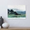 Abstract Mountain Landscape Painting with brlue and green marbled mountains against a white sky and white water, hung on a white wall above a natural wood shelf with a black vase, a white vase and a small stack of books