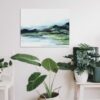 Abstract Mountain Landscape Painting with brlue and green marbled mountains against a white sky and white water, hung on a white wall above a green potted plant and white furniture