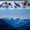 large landscape painting with textured flowing blue mountains against a lavendar and pink sunset sky styled on a white table with bits of wood, crystals and leaves surrounding it