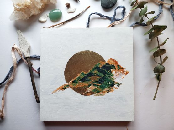 an abstract landscape painting with brown and green marbled paint in the shape of rugged mountains against a white background and a gold leaf moon.