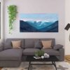 Blue textured Vancouver bc mountains against a lavendar and pink sky wall art print hung on beige wall above grey couch in a livingroom next to plants and a window