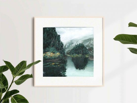 Misty tree painting with dark green trees on a grey lake painting in a square gold frame against a white wall with the leaves of two different plants around it